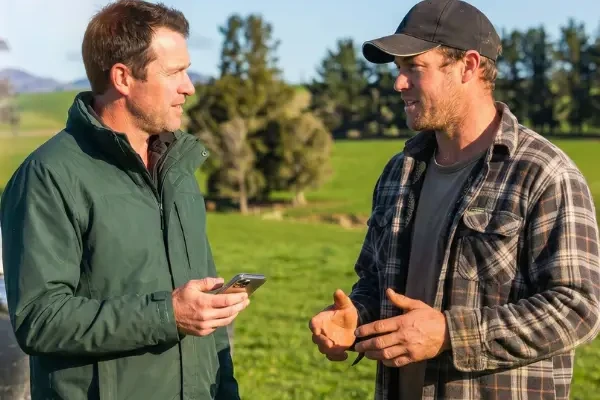 Two farmers talking in a paddock, one holding a phone